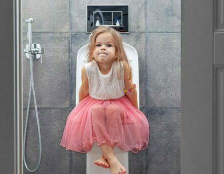 Ein kleines Mädchen im Rosa Kleid sitzt mit angestrengt verzogener Mine auf einer modernen Toilette