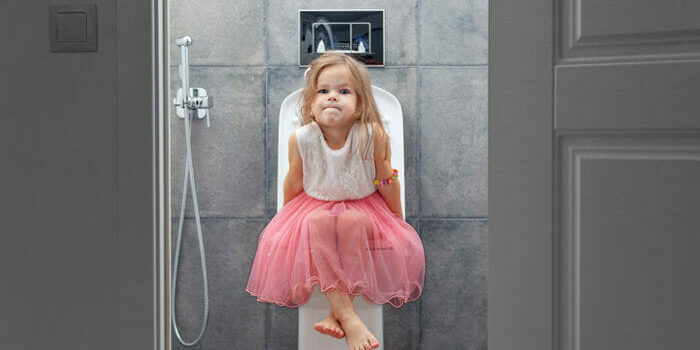 Ein kleines Mädchen im Rosa Kleid sitzt mit angestrengt verzogener Mine auf einer modernen Toilette