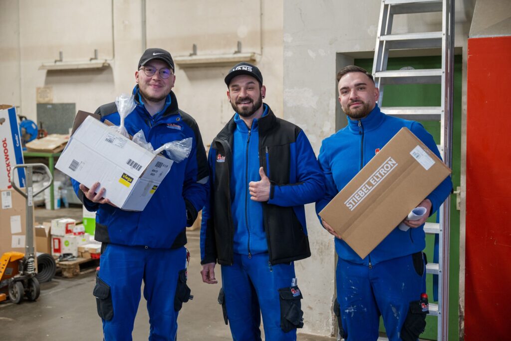 Drei Mitarbeiter in Arbeitskleidung lächeln in die Kamera