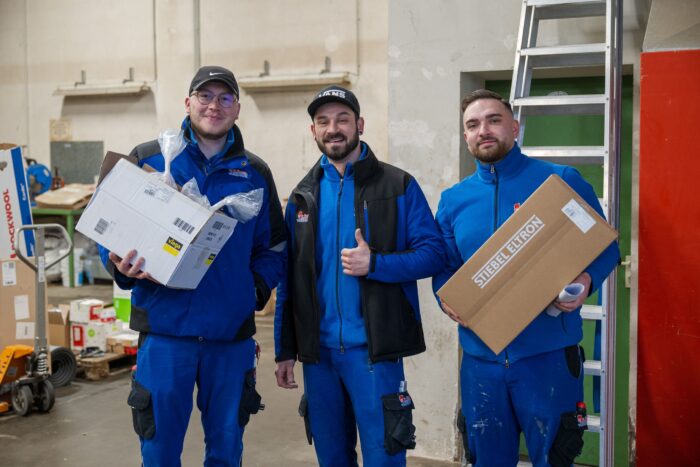 Drei Mitarbeiter in Arbeitskleidung lächeln in die Kamera