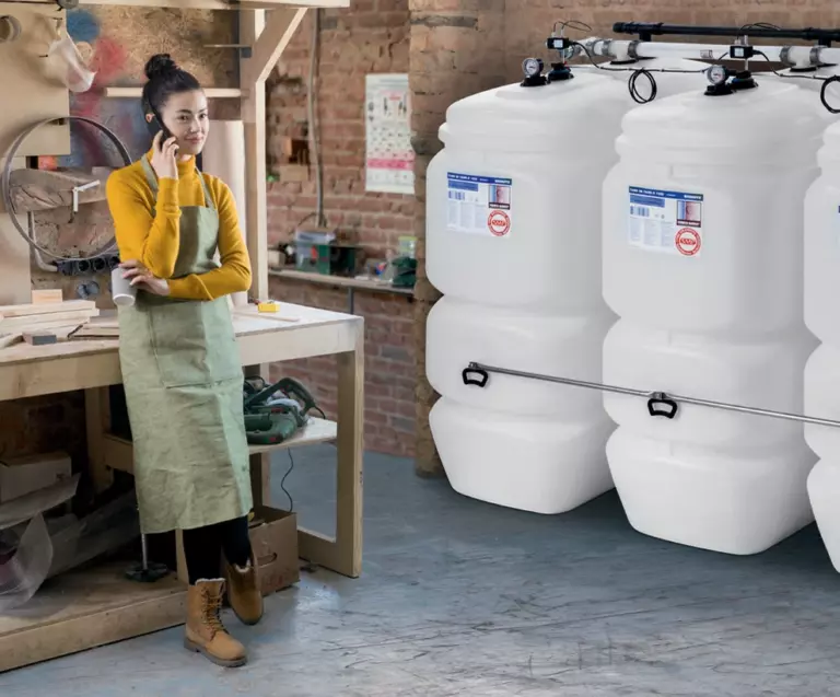 Junge Dame im Arbeitsoutfit lehnt an einer Werkbank. Im Hintergrund einige Öltanks