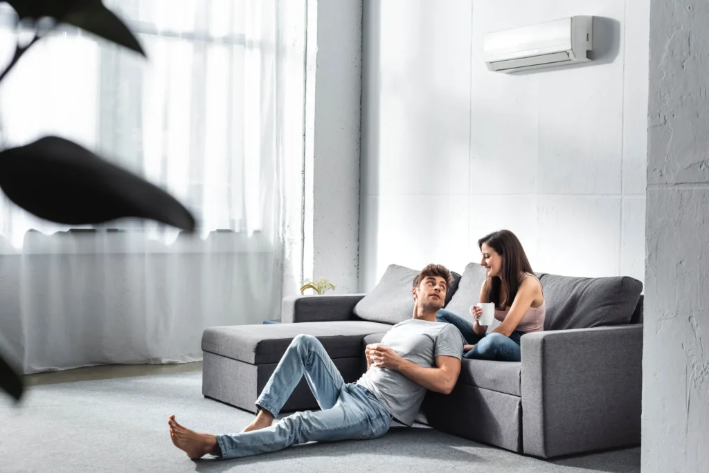 Ein junges Paar sitzt auf dem Sofa, an der Wand über ihnen hängt eine Klimaanlage